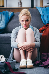sad woman sitting with scattered clothes after breaking up with boyfriend and looking at camera