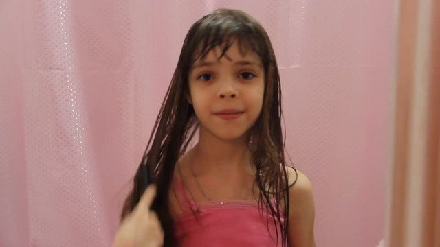 Cute and beautiful smiling girl combs her long wet hair.