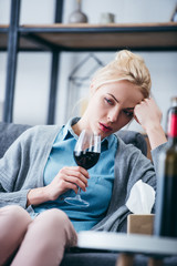 upset woman sitting with glass of red wine and tissue box at home
