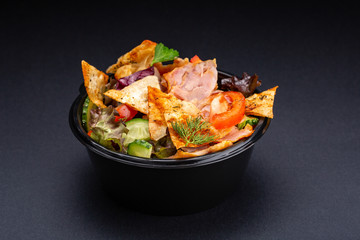 Salad served on black background. Restaurant dish concept. Dish in restaurant - salad with tomatoes, arugula, lettuce, cheese, almond chips, radicchio, fried meat.