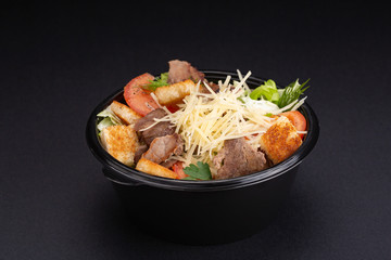 Salad with beef, spinach, tomatoes and Parmesan cheese. On a black background.