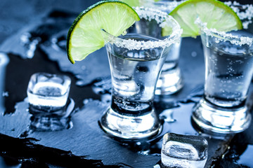 Fototapeta na wymiar Silver tequila shots with ice and lime on black table background