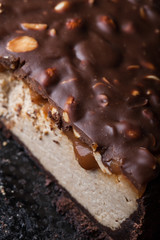 Close up view of a piece of peanut butter chocolate caramel cheesecake pie and cup of coffee on wooden background with a coffee pot and cheesecake in the background. A Sweet Coffee Break concept 