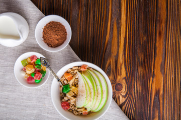 Breakfast bowl of oat granola with apple and dry fruit in a white bowl on brown wooden background  with a yogurt. Copy space