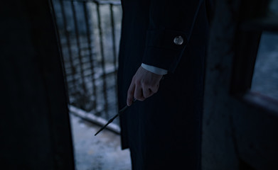 Young man in image of black magician with magic wand in his hand.