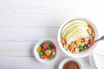 Breakfast bowl of oat granola with apple and dry fruit in a white bowl on white wooden background  with a yogurt. Copy space
