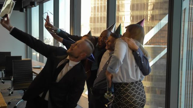 Happy employees celebrating boss's birthday at the office and making selfie photos. Good relationships with bosses. Daylight, smiles and dancing in holiday caps. 4k Slow Motion.