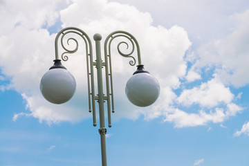 Two spherical streetlamp on white vintage pillar on background of big cloud in blue sky. Streetlight with copy space. Street lamp close-up.