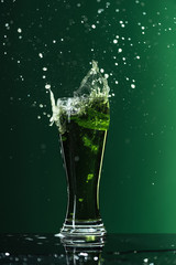 glass of beer with splashes isolated on green, st patrick day concept