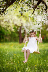Naklejka na ściany i meble Cute young girl having fun on a swing in blossoming old apple tree garden. Sunny day. Spring outdoor activities for kids