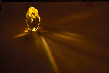 Rays of light passing through a large yellow quartz crystal on a dark brown background.
