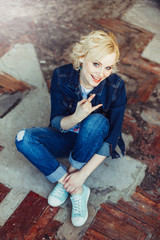 Hipster positive young caucasian blondie woman sitting on a wooden floor 