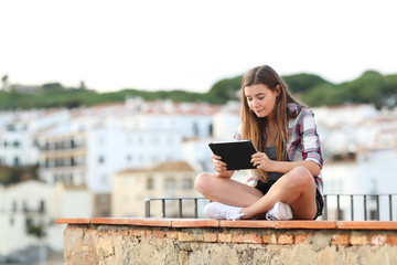 Serious girl using a tablet sitting on a ledge