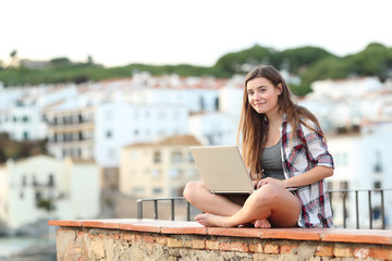 Teenage girl looking at camera using a laptop in a town