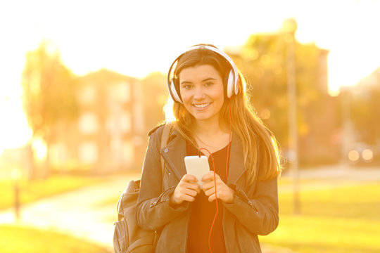 Happy teenage girl listening to music looking at you
