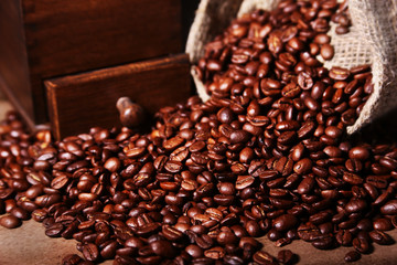 Fresh roasted coffee beans in burlap sack, coffee cup and grinder on dark background.