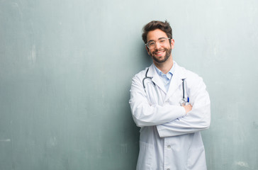 Young friendly doctor man against a grunge wall with a copy space crossing his arms, smiling and happy, being confident and friendly