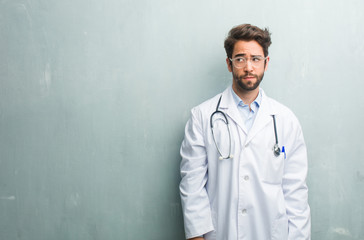 Young friendly doctor man against a grunge wall with a copy space doubting and confused, thinking of an idea or worried about something