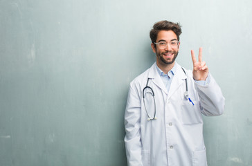 Young friendly doctor man against a grunge wall with a copy space showing number two, symbol of counting, concept of mathematics, confident and cheerful
