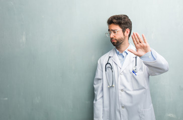 Young friendly doctor man against a grunge wall with a copy space serious and determined, putting...