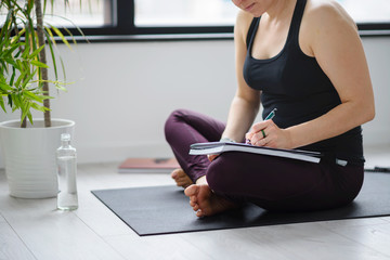Yoga woman writing in her notebook. Sitting at home by the window after exercise. Personal growth...