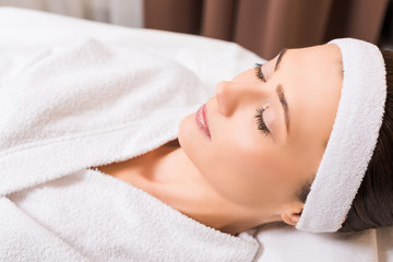 Obraz na płótnie Canvas woman lying in white bathrobe and closed eyes at beauty salon