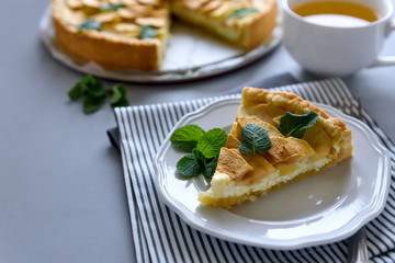 Homemade apple pie with cheese decorated mint leaves on gray wooden background. Teatime or vegetarian food concept. Selective focus.