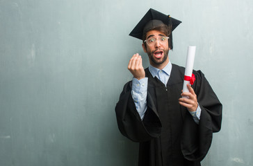 Young graduated man against a grunge wall with a copy space doing a typical italian gesture, smiling and looking straight ahead, symbol or expression with hand, very natural