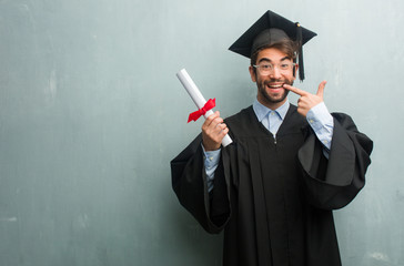 Young graduated man against a grunge wall with a copy space smiles, pointing mouth, concept of...