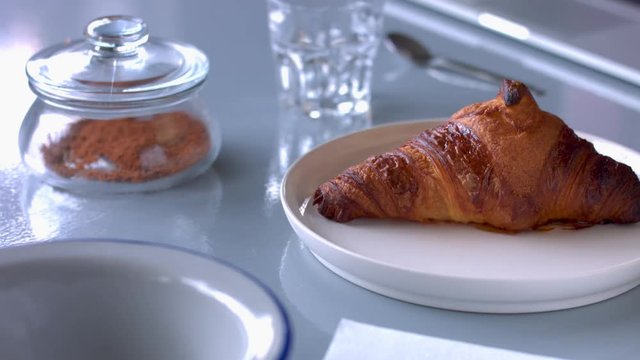 womans hand put a plate with croissant on the table and then serve some tea