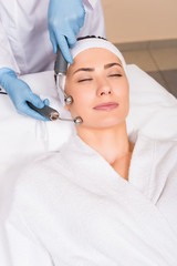 Naklejka premium beautician doing lifting with equipment on woman face at beauty salon