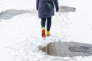 Winter Walk in Yellow Leather Boots. Back view on the feet of a women walking along the icy snowy...