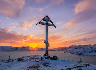 Sun Angel over the mount and Orthodox cross on the top of the snow capped mountain at sunrise.  Barents Sea coast at sunrise. Teriberka, Murmansk Region, Kola Peninsula. Russia
