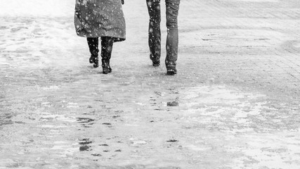 Winter City Slippery Sidewalk. Back view on the feet of people walking along the icy snowy...