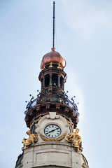 Reloj en torre de edificio con esculturas doradas.