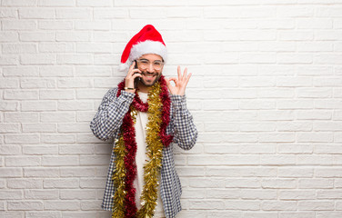 Young man sitting with gifts celebrating christmas cheerful and confident doing ok gesture