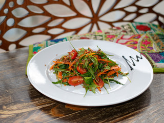 The vegetarian salad with vegetables, arugula and sprouted quinoa on white  plate on wooden table on background of openwork wood.