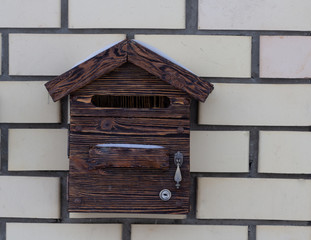 A beautiful wooden mailbox hangs on the wall of a brick house.