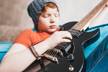 Closeup of a child playing a black electric guitar - hand picks up the notes on the strings - selective focus