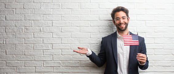 Young business man wearing a suit against a white bricks wall holding something with hands, showing a product, smiling and cheerful, offering an imaginary object - Powered by Adobe