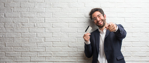 Young business man wearing a suit against a white bricks wall cheerful and smiling pointing to the front