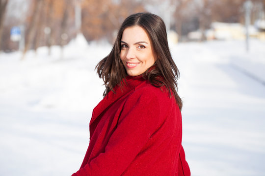 Young beautiful brunette woman in red coat posing on winter park
