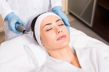 beatician holding darsonvalization equipment near woman face at beauty salon