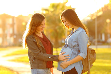 Happy pregnant woman showing belly to a friend