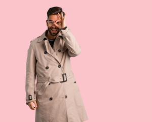 Young man wearing trench coat confident doing ok gesture on eye