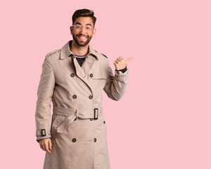Young man wearing trench coat pointing to the side with finger
