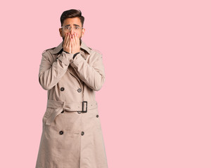 Young man wearing trench coat very scared and afraid hidden