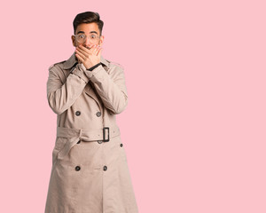 Young man wearing trench coat surprised and shocked