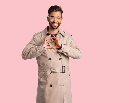 Young man wearing trench coat doing a heart shape with hands