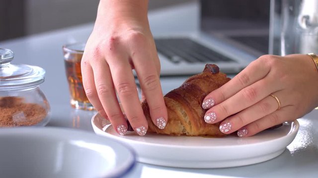 female hand splits a croissant in half
